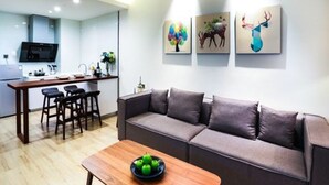Un salon moderne avec un canapé, une table basse sur laquelle on voit des pommes, et une cuisine en arrière-plan.