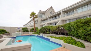 A swimming pool surrounded by greenery and a multi-story building with balconies.