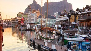 A harbor with boats docked, a waterfront building with a sign reading "CAPE UNION," and a mountain in the background.
