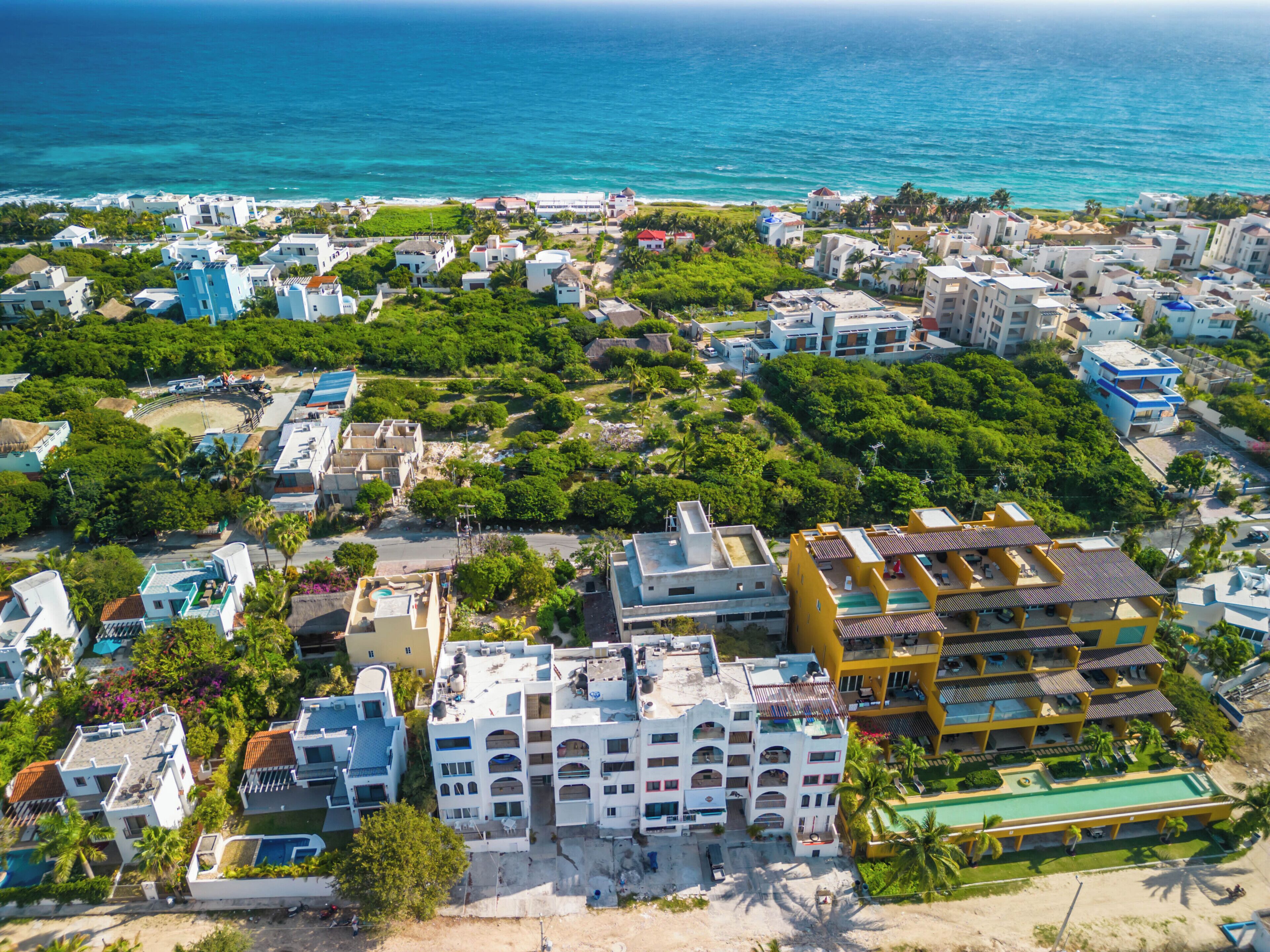 A coastal residential area with a mix of modern and traditional architecture, including a prominent multi-story building with balconies and a beachfront property.