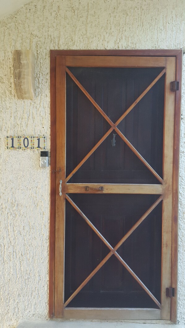 A wooden door with a cross-brace design, a house number plaque, and a small wall-mounted light fixture.