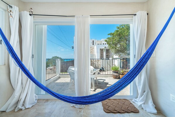 A room with a hammock, white curtains, a sliding glass door, and a view of the outside.