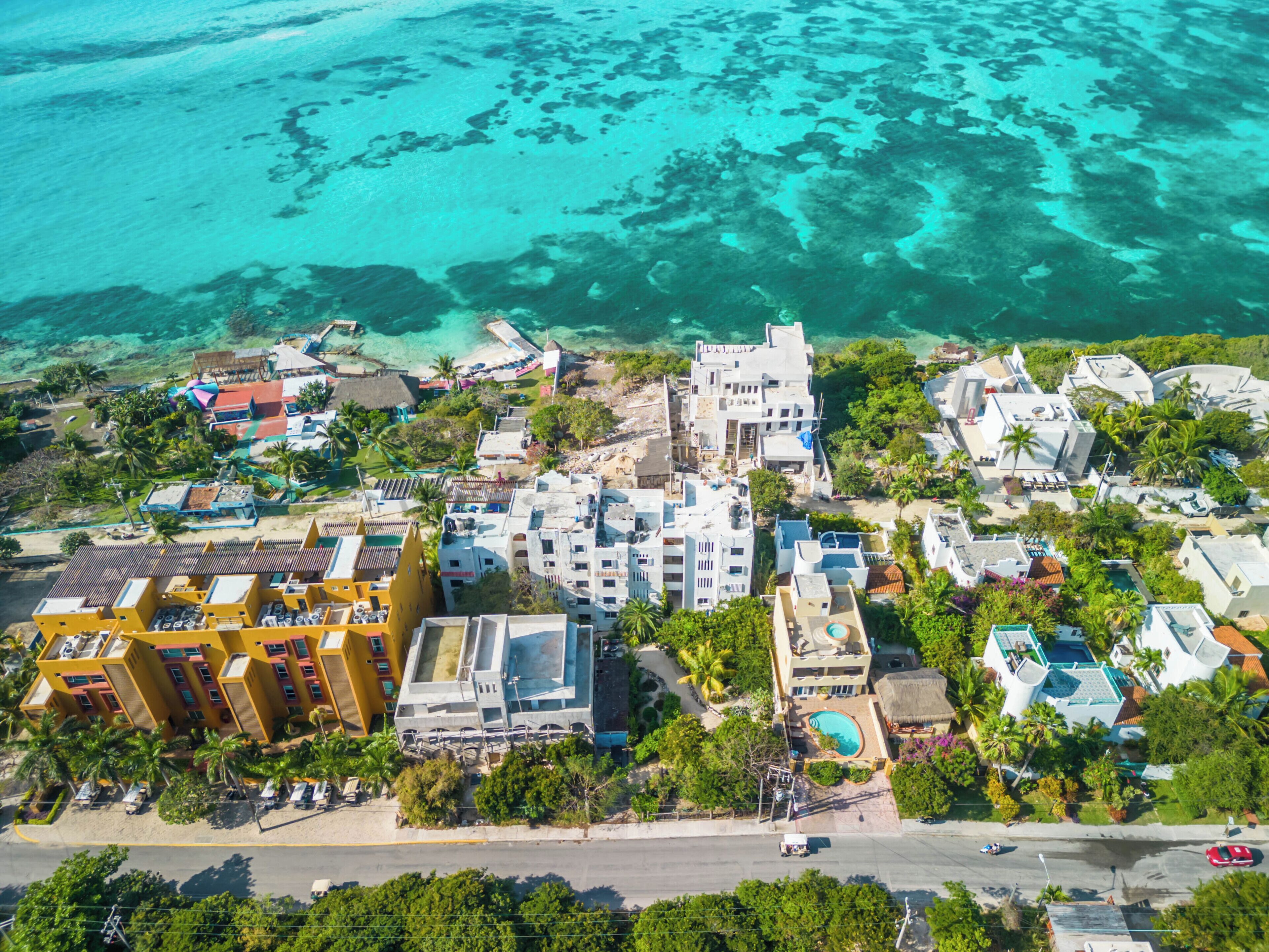 An aerial view of a coastal resort with buildings, a swimming pool, and clear turquoise waters.