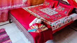 A room with a bed, red bedding, a fan, and a window with curtains. - Blessing Hotel (Jaisalmer)