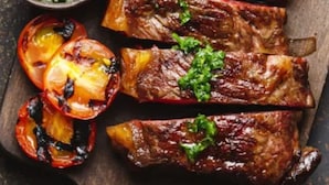 A wooden cutting board with grilled steak and roasted tomatoes, accompanied by a bowl of green sauce. - Blessing Hotel (Jaisalmer)