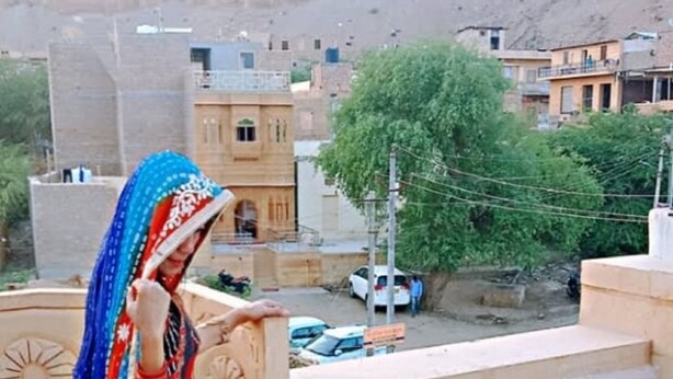 A person on a rooftop terrace with a view of buildings and trees. - Blessing Hotel (Jaisalmer)