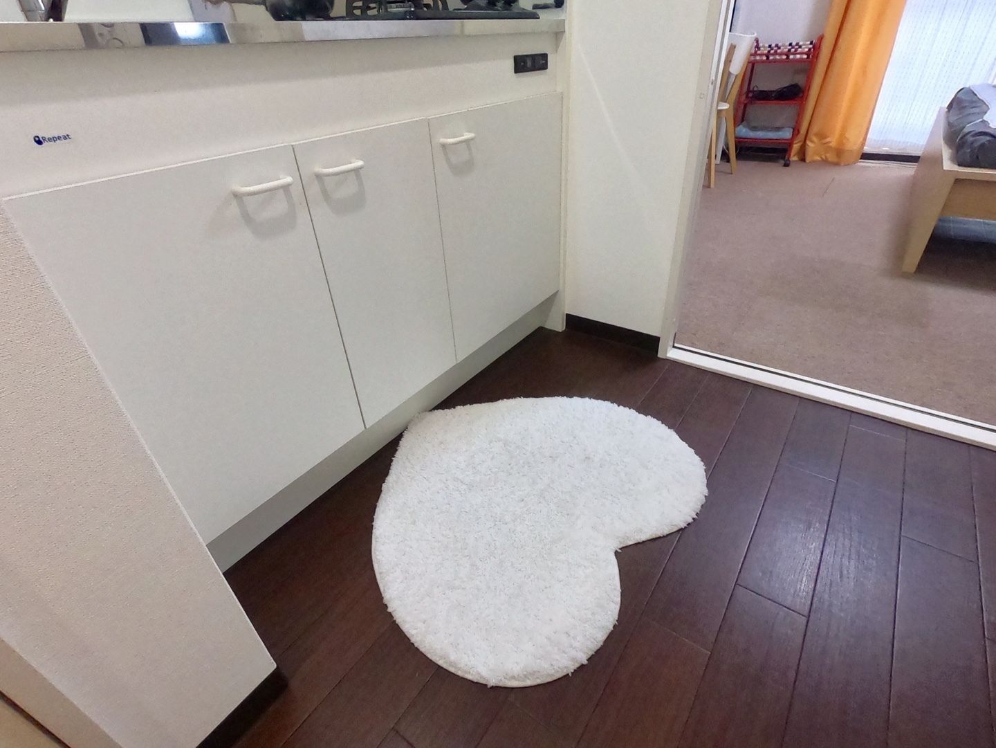 A kitchen with white cabinets, a white rug, and a wooden floor.