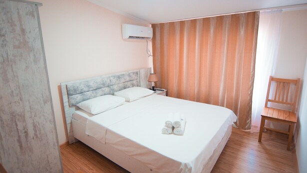 A neatly made bed with white linens and a headboard, a wooden chair, and a wall-mounted air conditioner. - Hotel Tsiskari (Telavi)