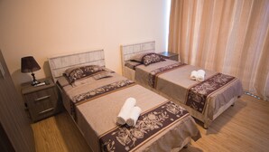 A hotel room with two single beds, each with a pillow and a rolled towel. There is a nightstand with a lamp and a remote control. - Hotel Tsiskari (Telavi)