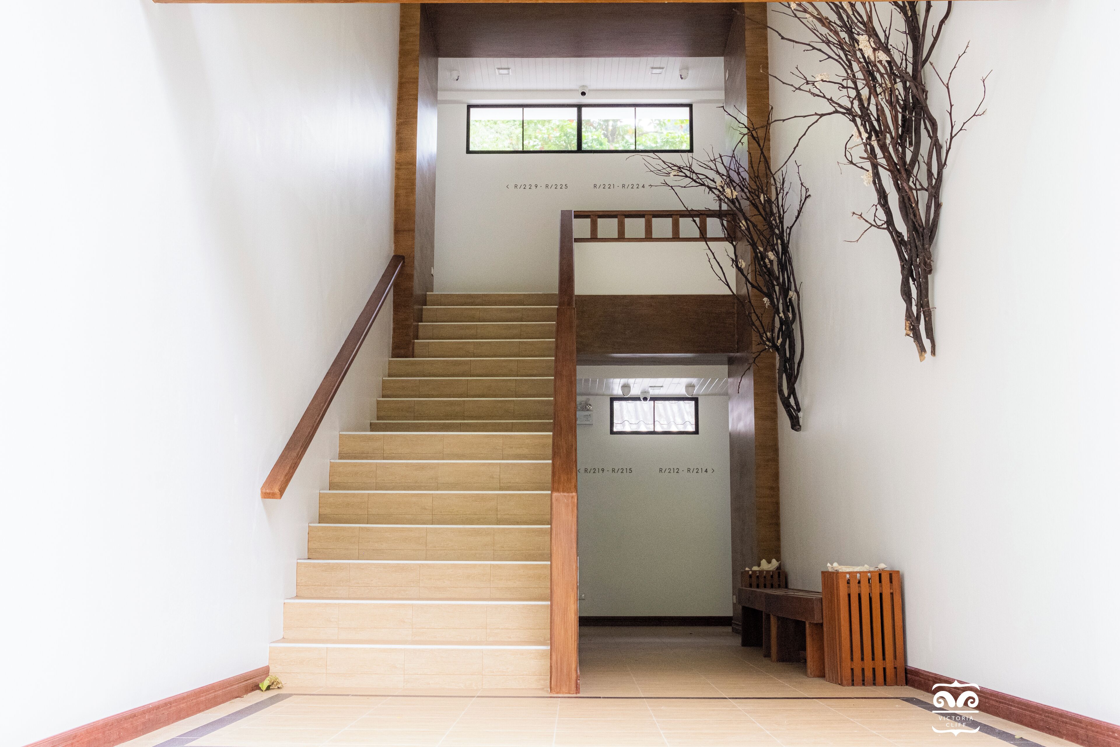 A staircase with wooden steps and a wooden handrail, leading to a landing with a bench and a wall-mounted decorative branch.
