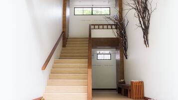 A staircase with wooden steps and a wooden handrail, leading to a landing with a bench and a wall-mounted decorative branch.