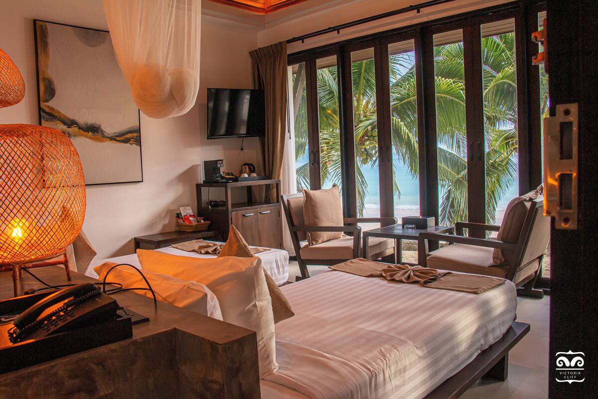 Ein Hotelzimmer mit Bett, Schreibtisch, Stuhl, Fernseher und Blick auf Palmen.