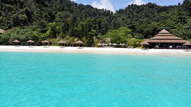 A beach resort with clear turquoise waters, thatched-roof huts, and lush greenery in the background. - Victoria Cliff Nyaung Oo Phee Island (Kawthaung)