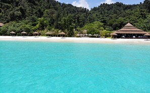 A beach resort with clear turquoise waters, thatched-roof huts, and lush greenery in the background. - Victoria Cliff Nyaung Oo Phee Island (Kawthaung)