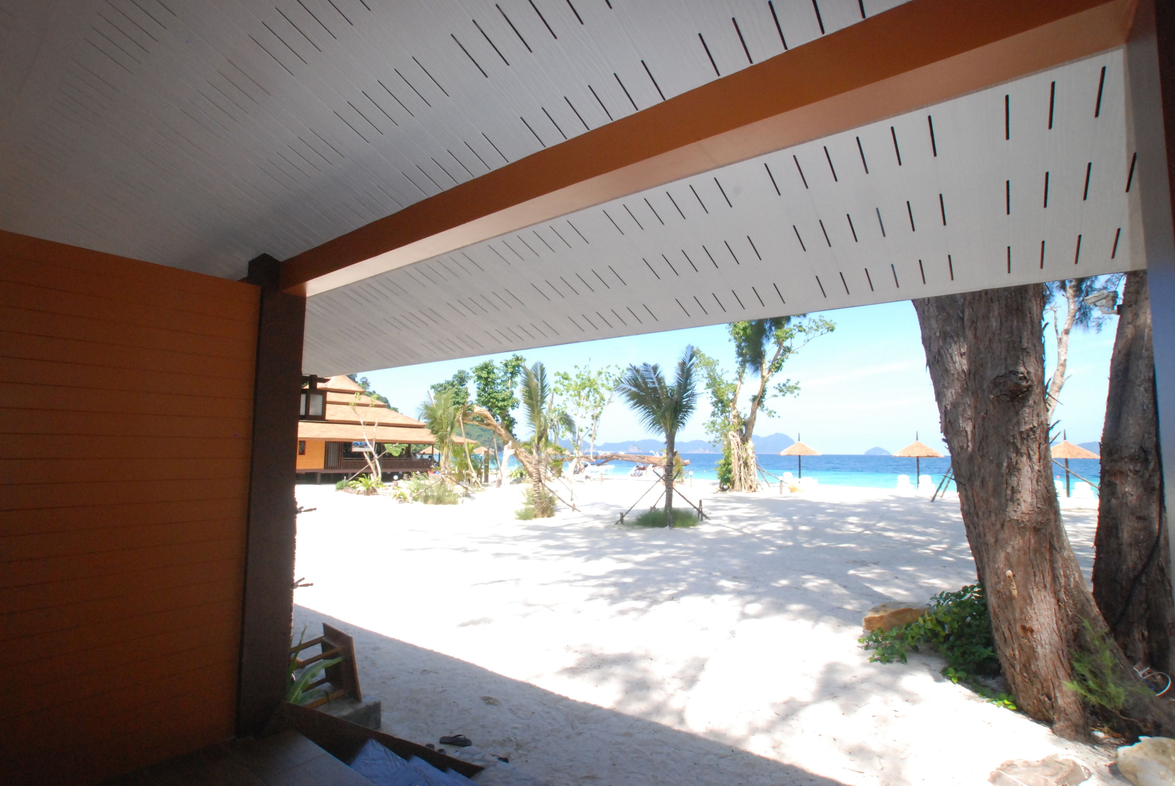Un espacio al aire libre techado con vistas a una playa de arena y palmeras.