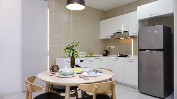 Una cocina moderna con armarios blancos, un refrigerador de acero inoxidable y un comedor con una mesa redonda y sillas.