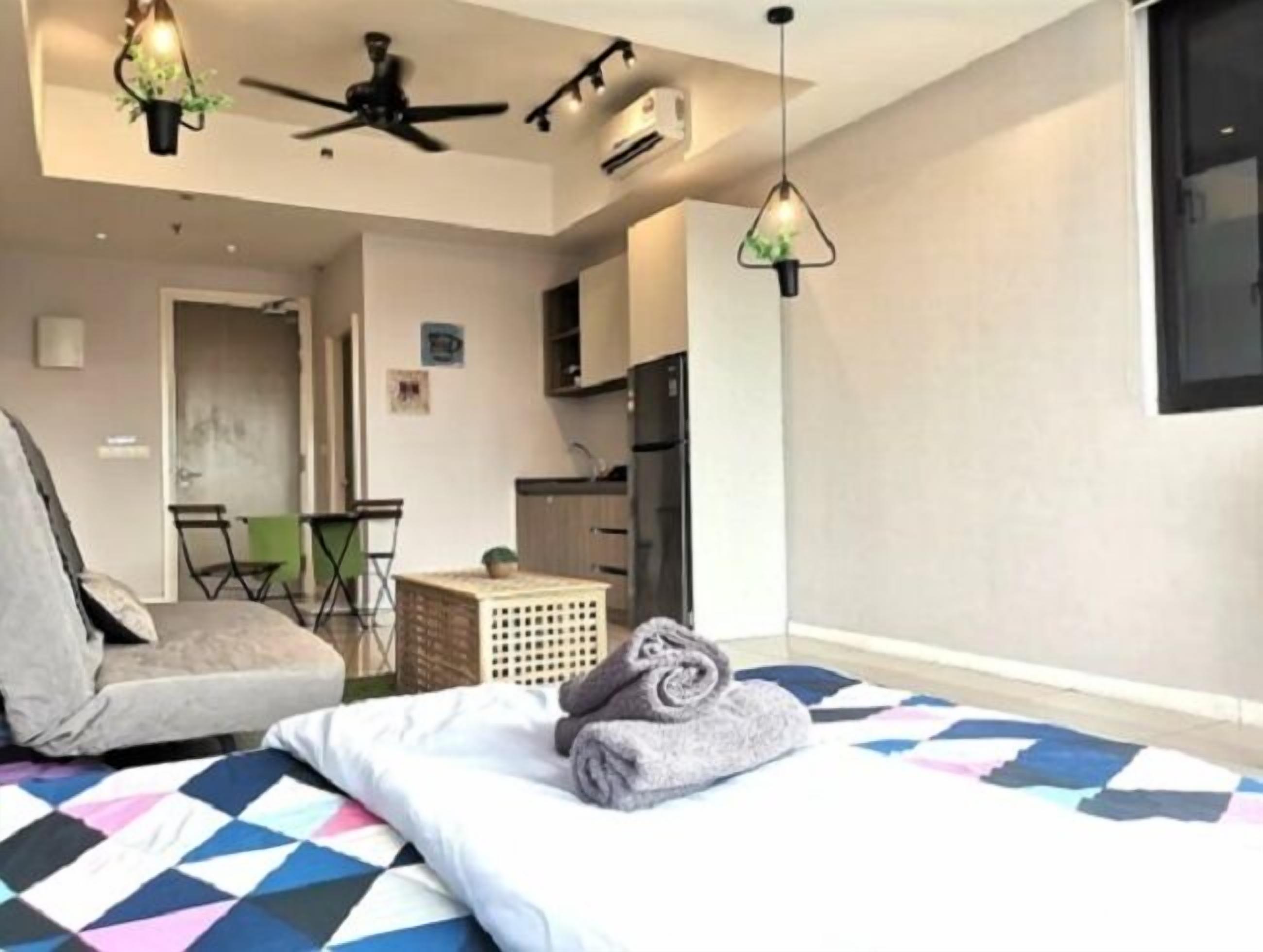 A compact bedroom with a bed, a chair, a small table, and a kitchenette.