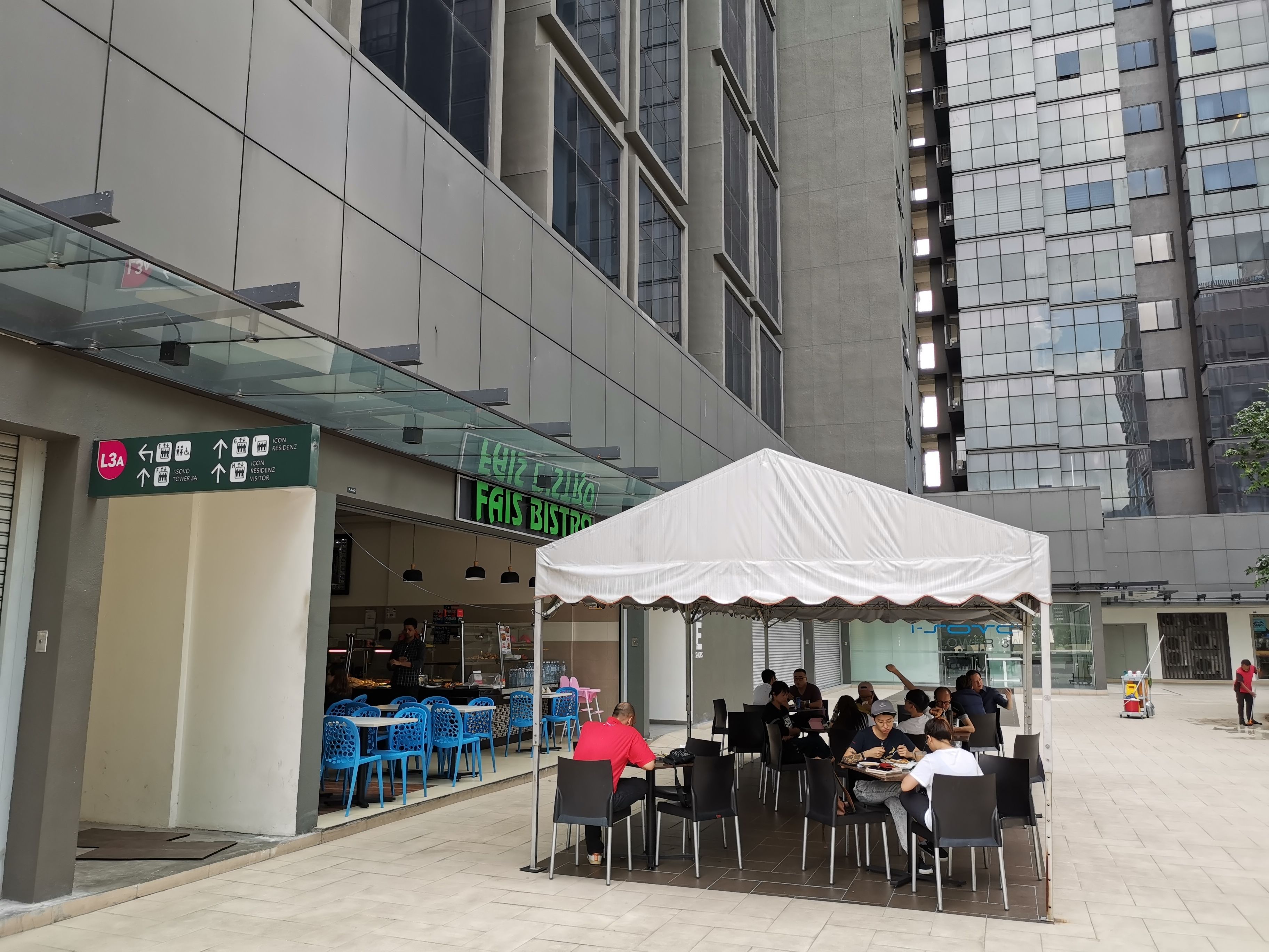 An outdoor café with tables and chairs, a white canopy, and a building with a sign reading "Fais Bistro".