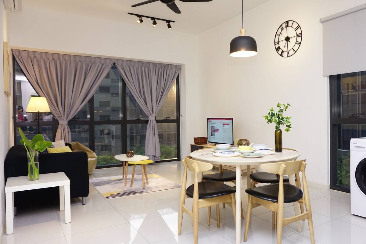 A modern living room with a dining area, a washing machine, and a large window with curtains.