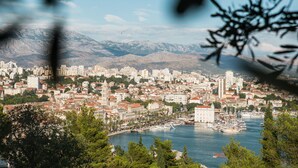 Un paysage urbain côtier avec un port de plaisance, des bâtiments et des montagnes en arrière-plan.