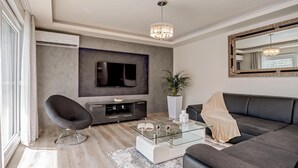 Un salon moderne avec un téléviseur à écran plat, une table basse en verre, un canapé noir et un grand miroir.