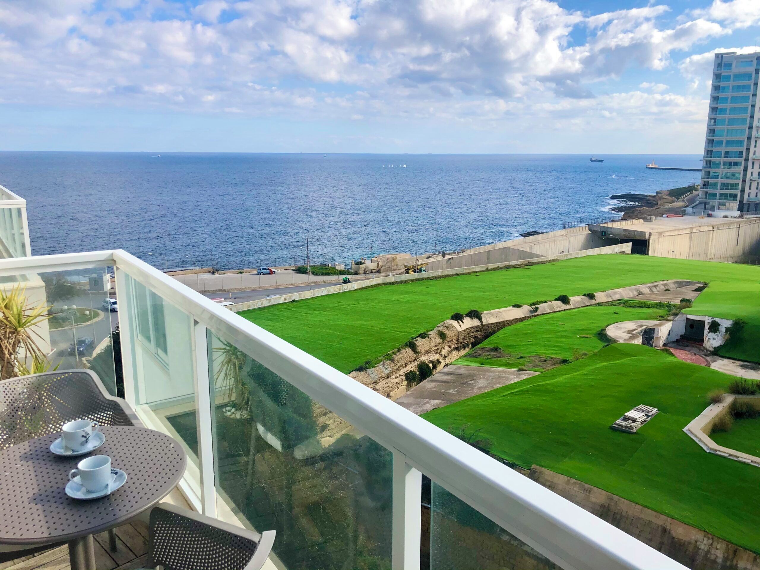 Un balcon donnant sur la mer, une pelouse et un bâtiment en arrière-plan.