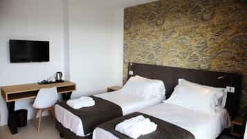 A hotel room with two beds, a desk, and a TV.