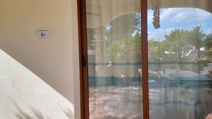 A sliding glass door with a decorative curtain, a small sign on the wall, and a view of an outdoor patio area with potted plants and a tiled floor. - Aquamarine villa with garden and wifi (San Teodoro)