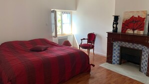 A bedroom with a large bed, a chair, a fireplace, and a window with curtains.
