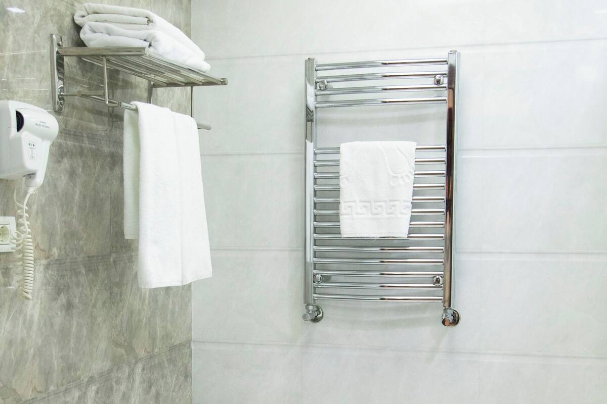 A modern bathroom with a white toilet, a towel rack, and a hairdryer on a wall-mounted shelf.