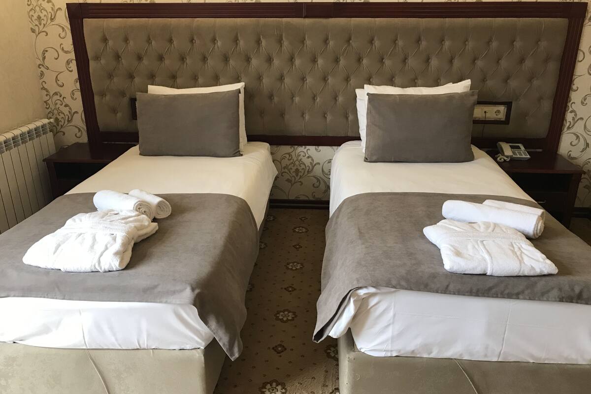 A double room with two beds, each with a grey bedspread and white pillows, and a wooden headboard. There are towels on each bed.