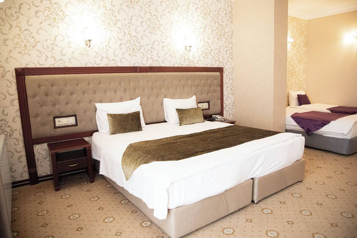 A hotel room with a large bed, a nightstand, a lamp, and a mirror.