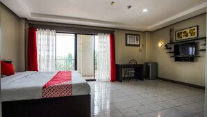 A hotel room with a bed, a desk, a television, and a balcony with curtains. - OYO 192 Tcc Condo - Hostel (Davao)