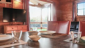 Ein Interieur einer Holzhütte mit Esstisch für zwei Personen, einem Fernseher und Blick ins Freie.