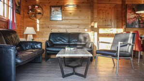 Ein gemütliches Blockhaus-Interieur mit Holzausstattung, einer schwarzen Ledersofa, einem passenden Sessel und einem kleinen Holztisch.