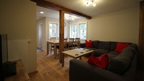 Ett vardagsrum med en mörkgrå soffa, röda kuddar, ett träbord och en matplats med trästolar och ett bord.