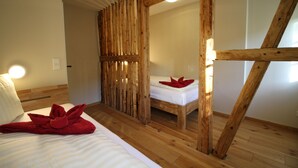 Ett rum med träram, en säng och ett litet bord, en trävägg som avskärmning och en lampa på väggen.