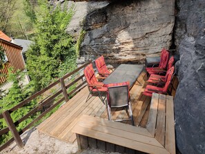 A wooden deck with a table and chairs, surrounded by a rocky cliff and greenery. - Felsenkeller Bielatal "Johanniswacht" (Rosenthal-Bielatal)