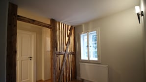 Une pièce avec des poutres en bois, une porte blanche, une fenêtre donnant sur un beau paysage et un radiateur.