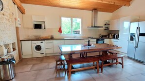 Una cocina con una mesa de madera, bancos, lavadora, microondas y refrigerador.