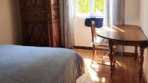 Una habitación con una cama, un armario de madera, una mesa y un ventanal con cortinas.