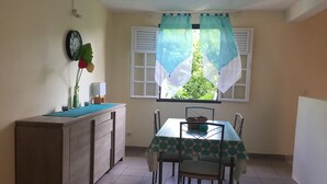 Ein kleiner Essbereich mit Tisch und Stühlen, einem Schrank, einer Uhr und einem Fenster mit Vorhang.