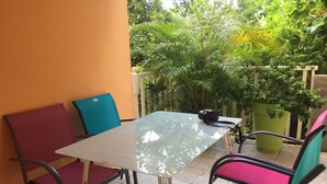 Eine Terrasse mit einem Glastisch, zwei roten Stühlen und zwei grünen Stühlen.