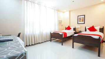 A hotel room with two beds, a desk, and a window with curtains.