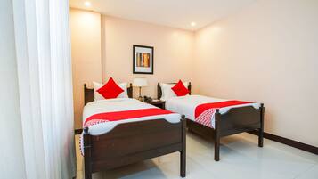 A hotel room with two wooden beds, white bedding, red pillows, a nightstand with a lamp, and a framed picture on the wall.
