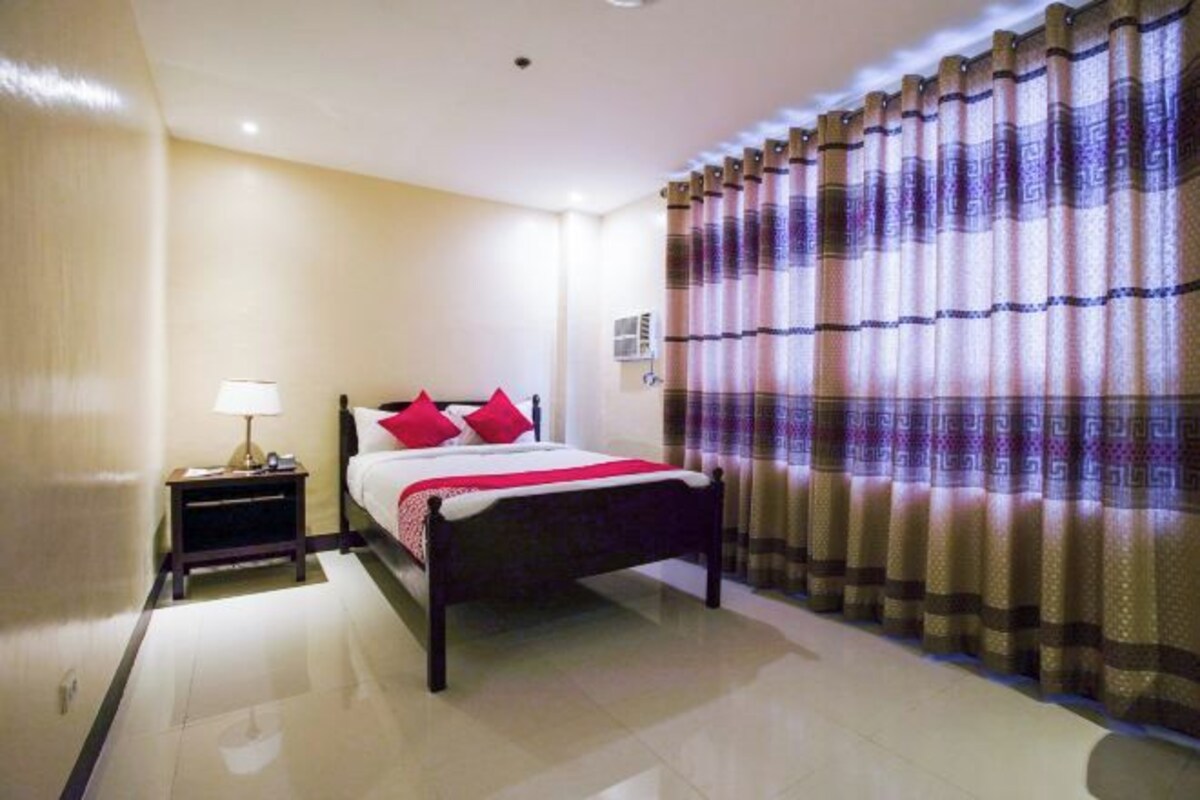 Una habitación de hotel con cama, mesita de noche, lámpara y cortinas.