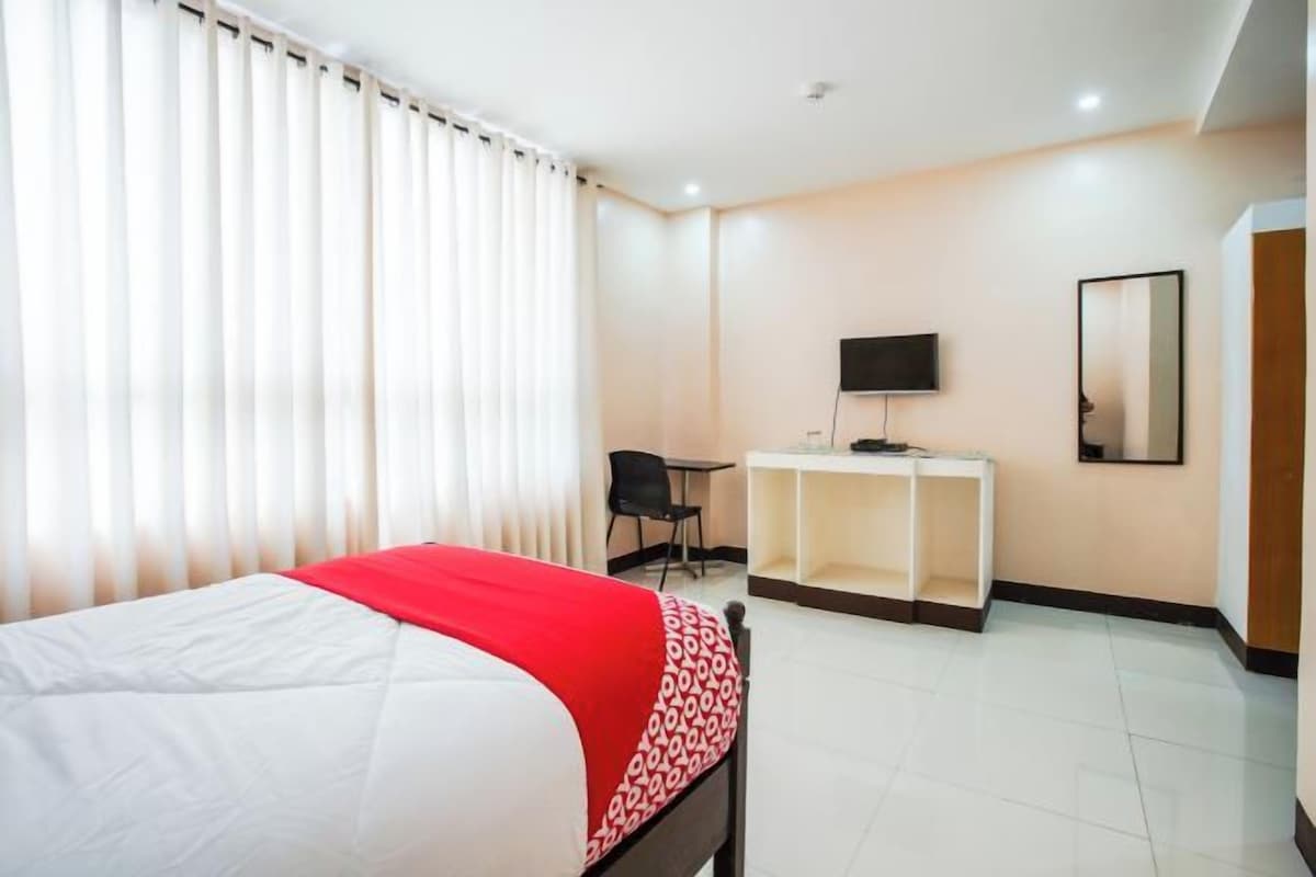 Una habitación de hotel con una cama, un escritorio con silla, un televisor y un espejo en la pared.