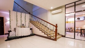 A spacious living area with a staircase, a dining table set with white tablecloths, and a decorative arrangement.