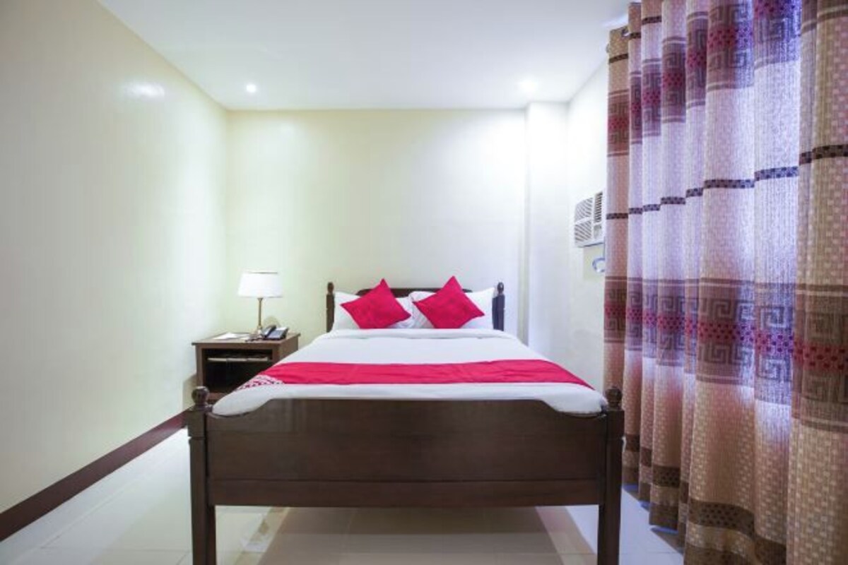 Una habitación de hotel con cama, mesita de noche y cortinas.