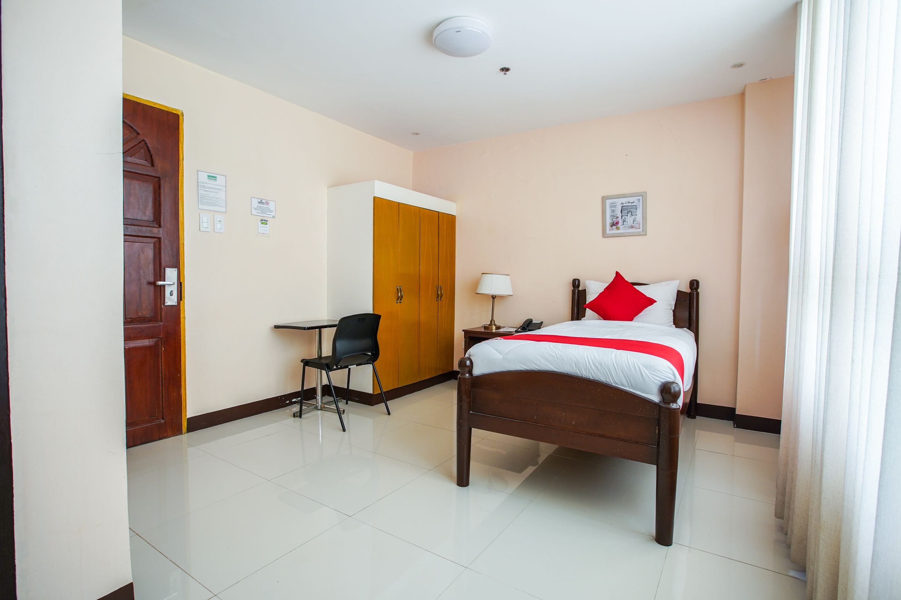 A hotel room with a wooden bed, a desk, a chair, and a wardrobe.